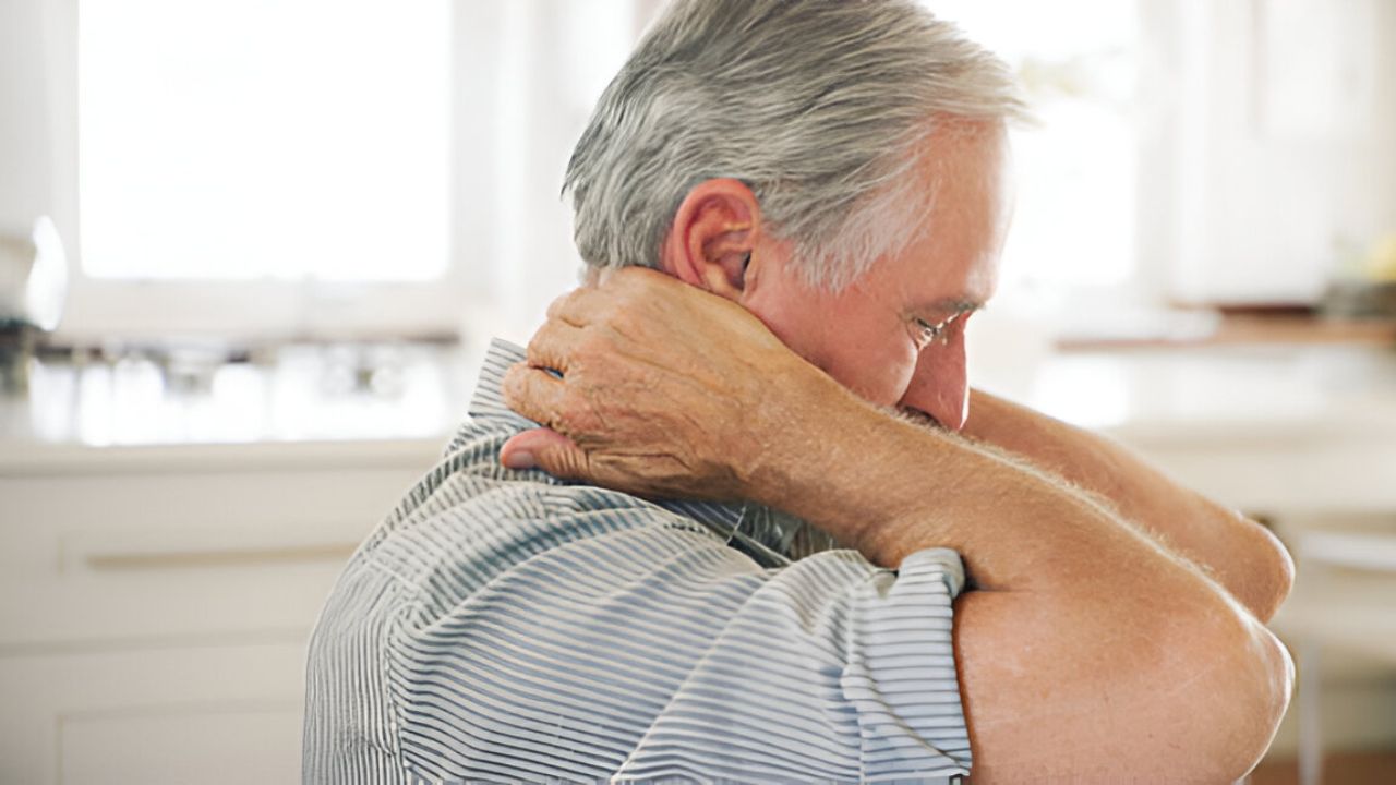 A mature individual with gray hair rubs their neck and upper back with both hands, appearing to experience discomfort, possibly related to sciatica treatment.