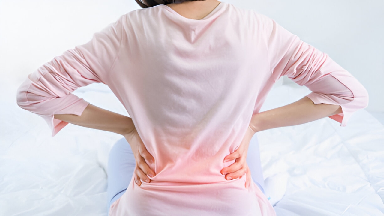 A female patient holds her lower back, highlighted with red, depicting back pain relief services at Ridgefield Chiropractic & Wellness Center.